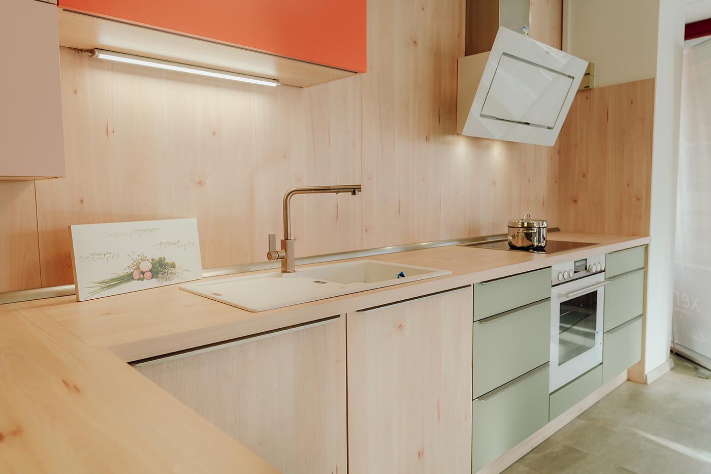 Küche aus Holz mit Fronten in orange & mintgrün in der Küchenausstellung Matthäs