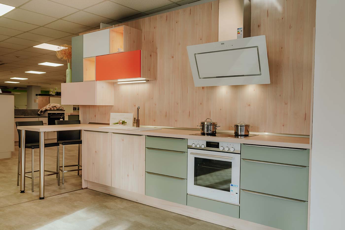 Küche aus Holz mit Fronten in orange & mintgrün und weißer Dunstabzugshaube in der Küchenausstellung Matthäs